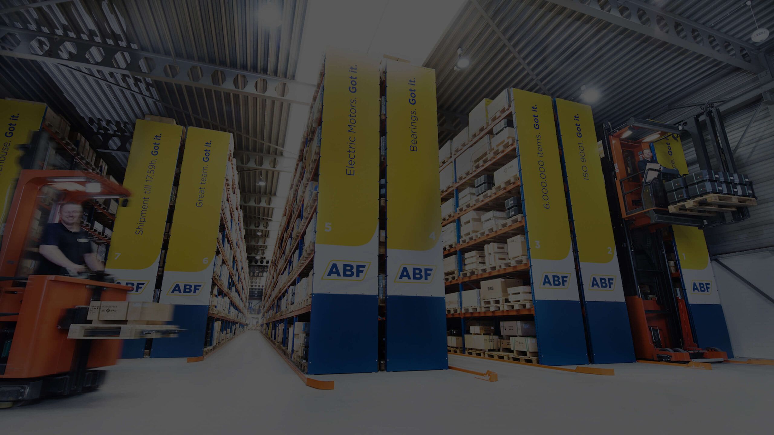 Een rode heftruck manoeuvreert vakkundig langs een ABF-medewerker tussen de hoge productplanken in het magazijn.