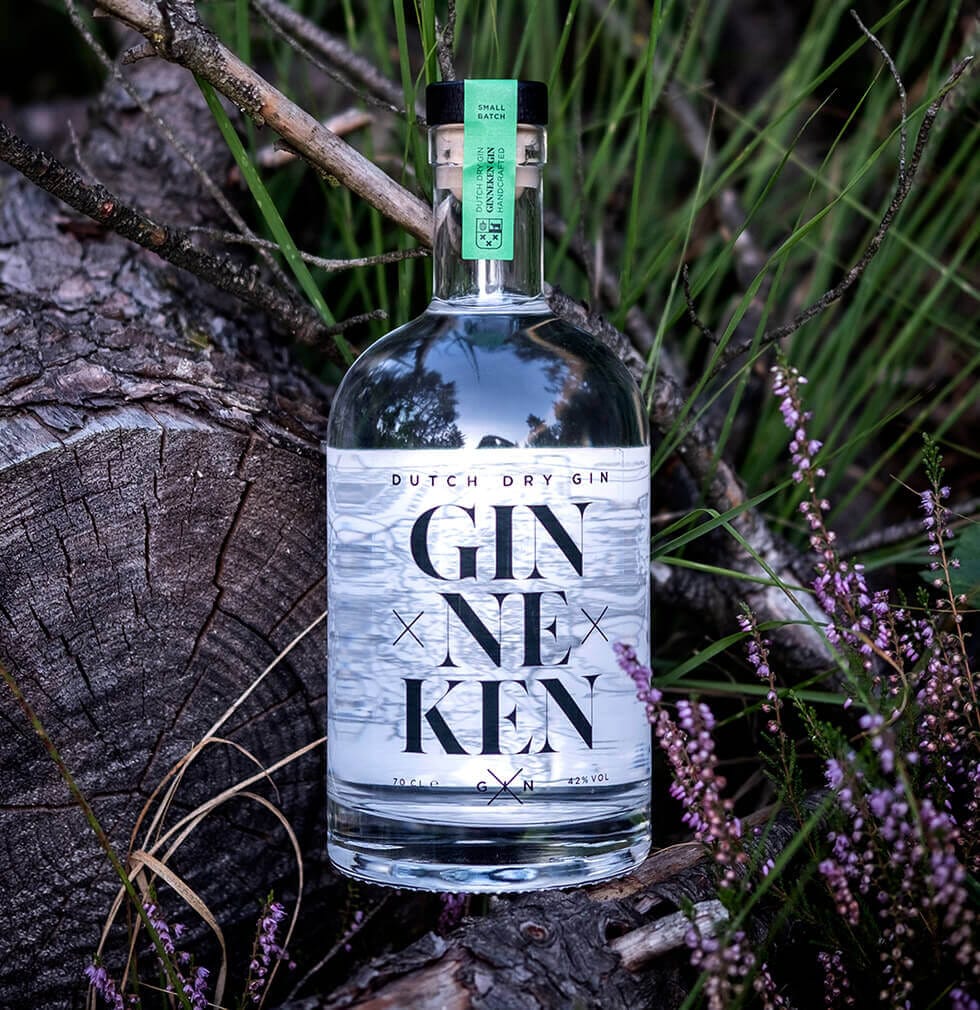 Een fles Nederlandse droge gin ligt stijlvol op boomstammen, tegen een achtergrond van groen gras en paarse bloemen.