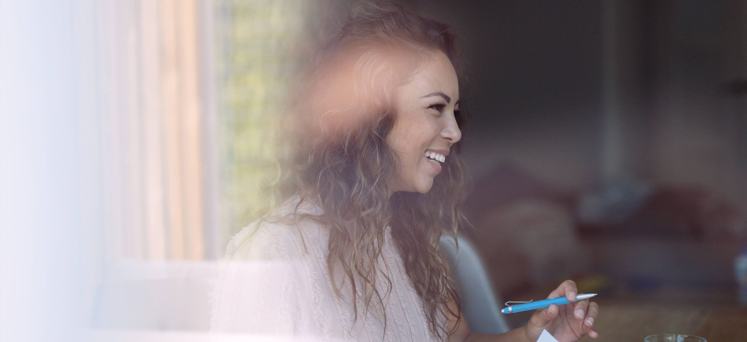 In een warm verlichte kamer staat een glimlachende vrouw met een pen in haar hand. Ze straalt de gezellige elegantie van de stijl van CS Wonen uit.