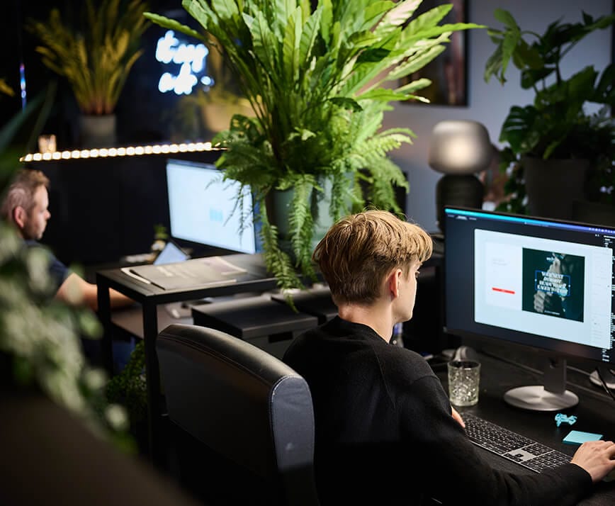 Werknemers achter computerbureaus, weelderige kamerplanten, moderne kantoorsfeer.