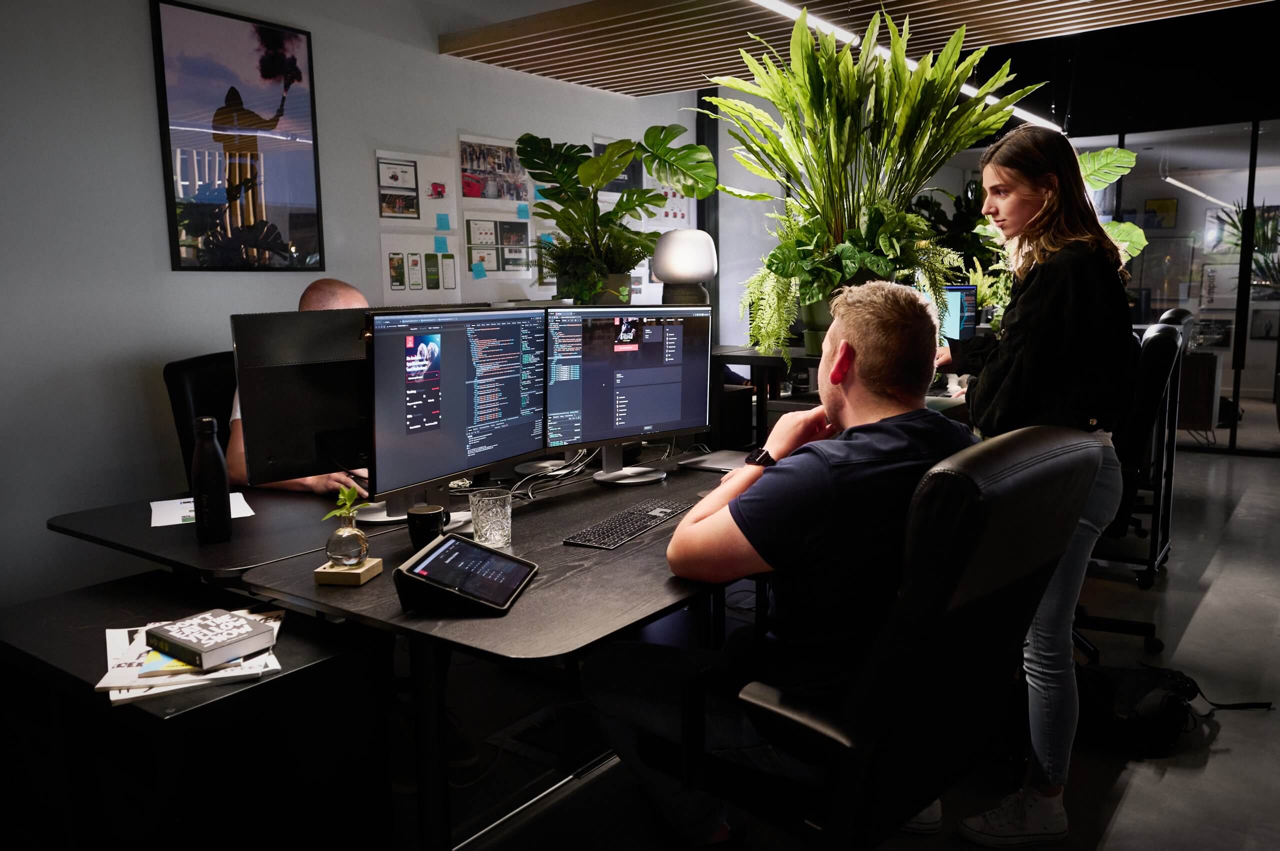 In een kantoor vol technologie en planten beheren drie mensen efficiënt koppelingen achter hun computers.
