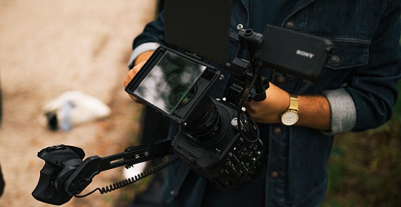 Videograaf in spijkerjack en kijkend naar de natuur, filmend in de buitenlucht met een professionele camera.