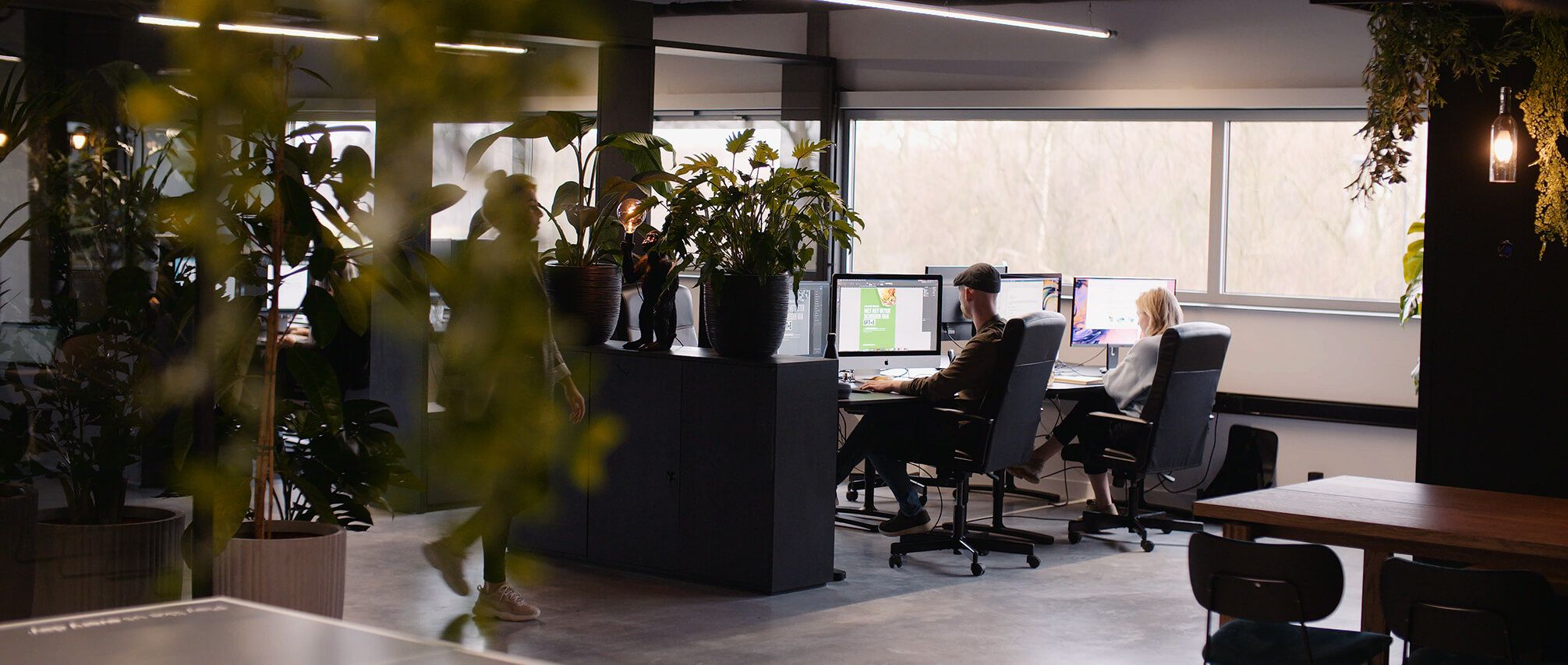 Hedendaags kantoor: bureaus, grote ramen en weelderige planten vullen de ruimte.