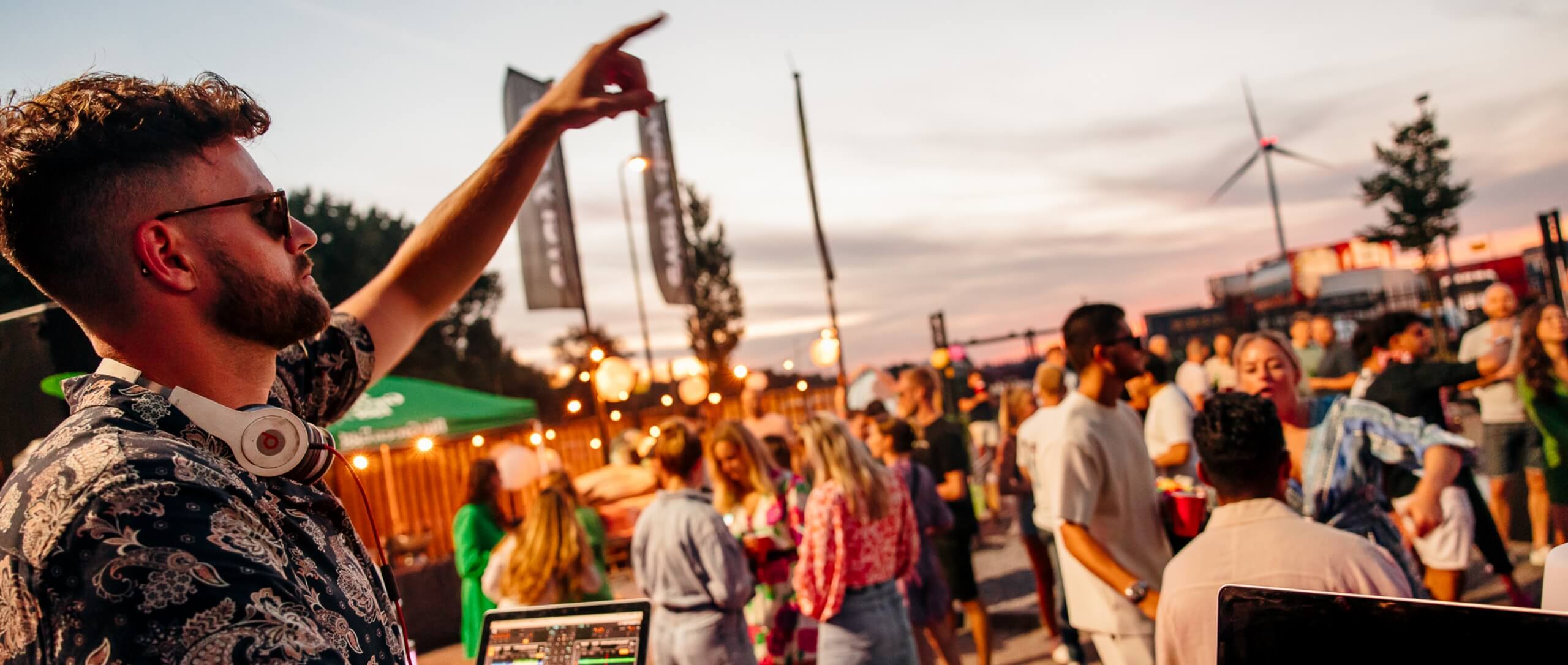 DJ draait op een bruisend buitenfeest, met een energiek publiek en warme avondverlichting.