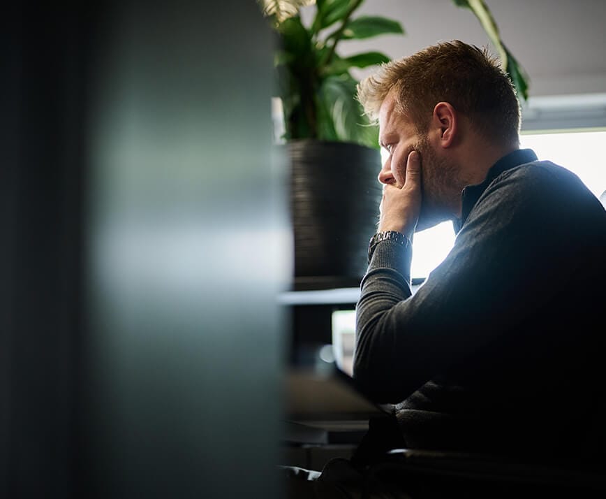 Man zit aan een bureau, nadenkend; plant op de achtergrond.