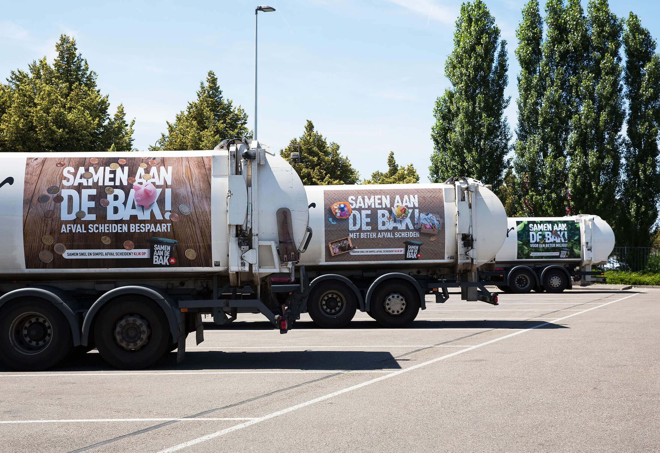 Vrachtwagens op het parkeerterrein tonen opvallende banners van de afvalscheidingscampagne Samen Aan De Bak!.