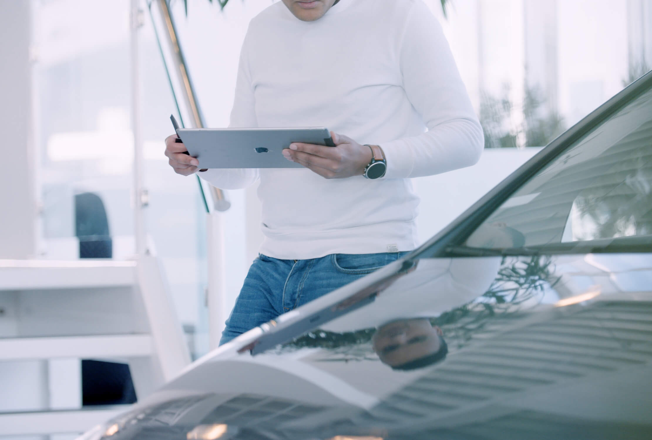 Op een helder verlicht kantoor gebruikt iemand in een wit overhemd de Car Collect-app op een tablet naast een auto.