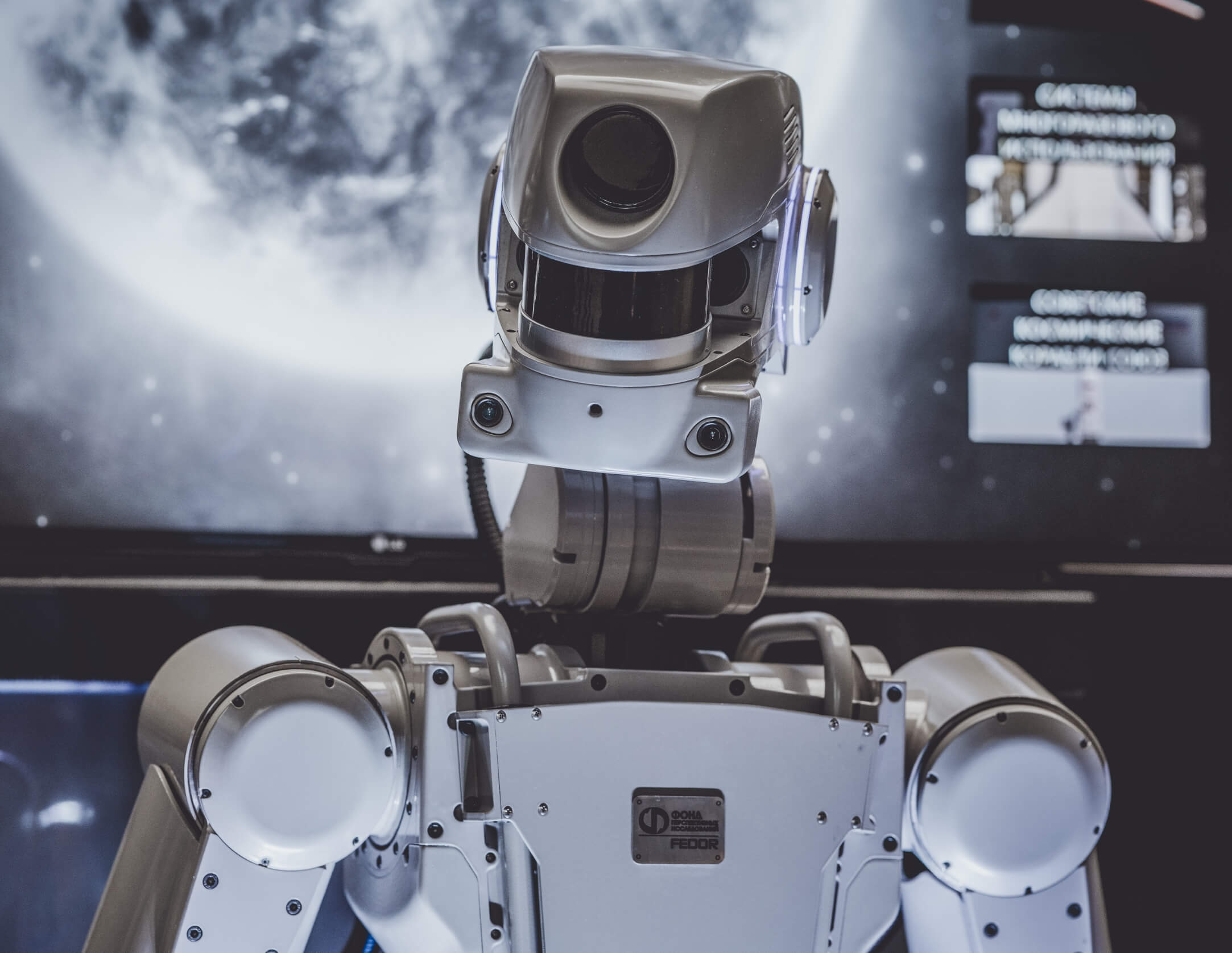 Een humanoïde robot staat voor een scherm waarop een grote afbeelding van de maan te zien is.