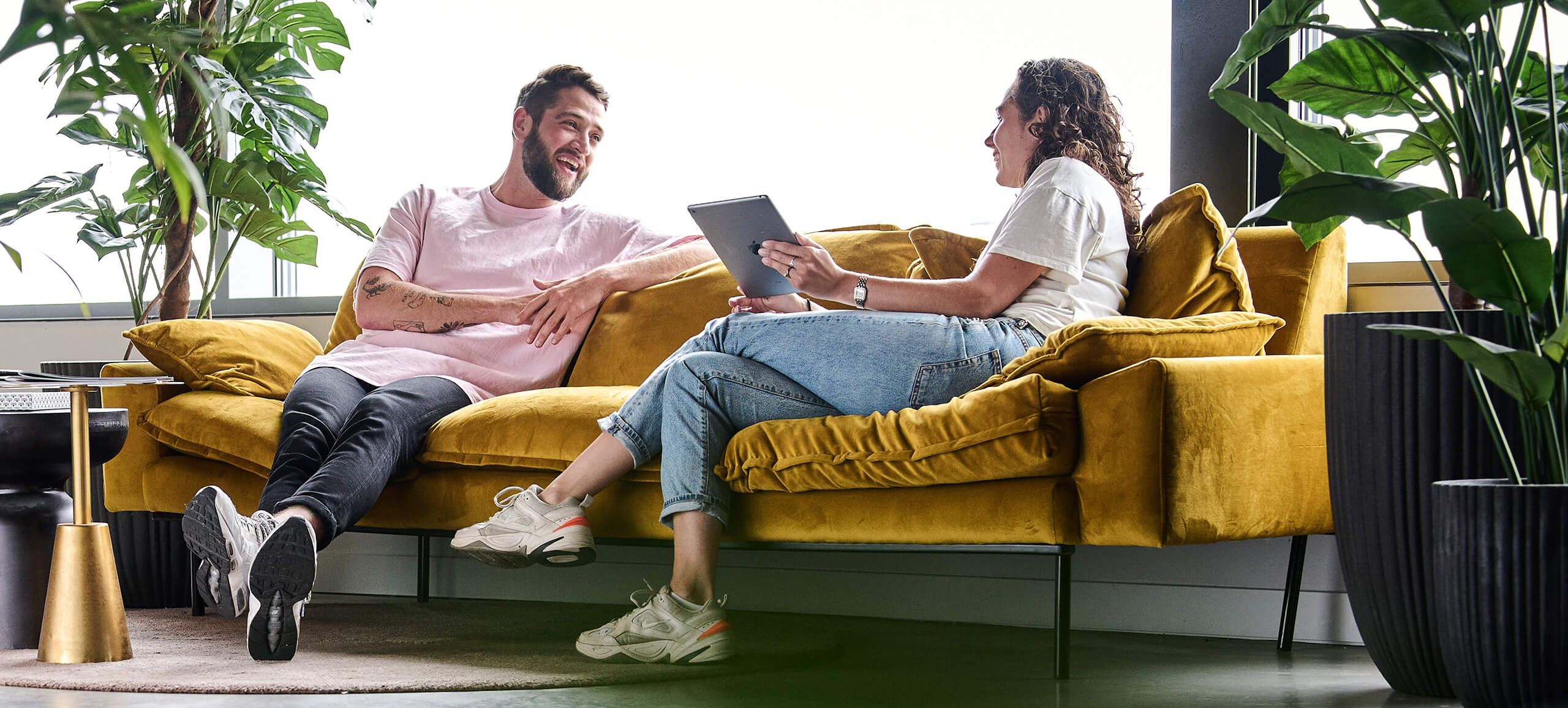 Twee mensen op een gele bank kletsen vrolijk en bespreken op een tablet strategieën voor leadgeneratie.