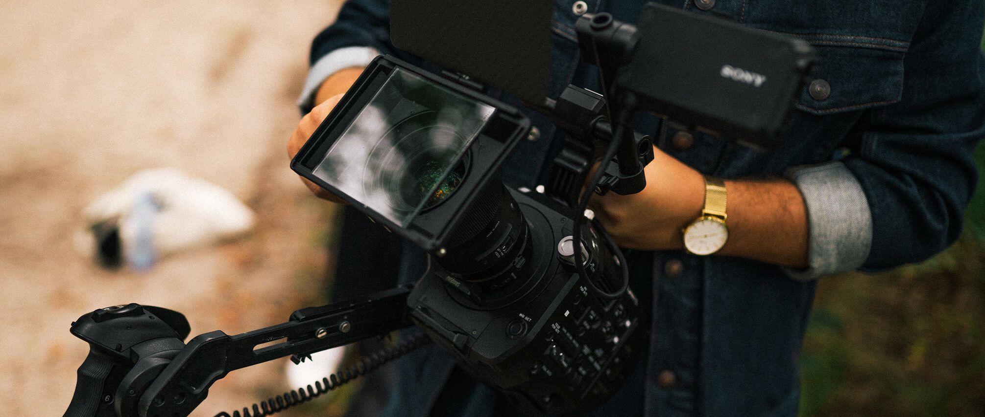 Een professional, gekleed in spijkerbroek, filmt outdoor-ontwerpen met grote scherpte, waarbij het camerascherm de reflectie van de lens laat zien.