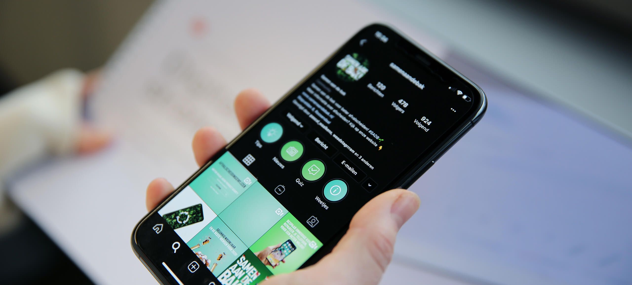 Iemand houdt een smartphone vast met daarop een Instagram-profiel vol foto's en pictogrammen, waarop zijn digitale strategie te zien is.