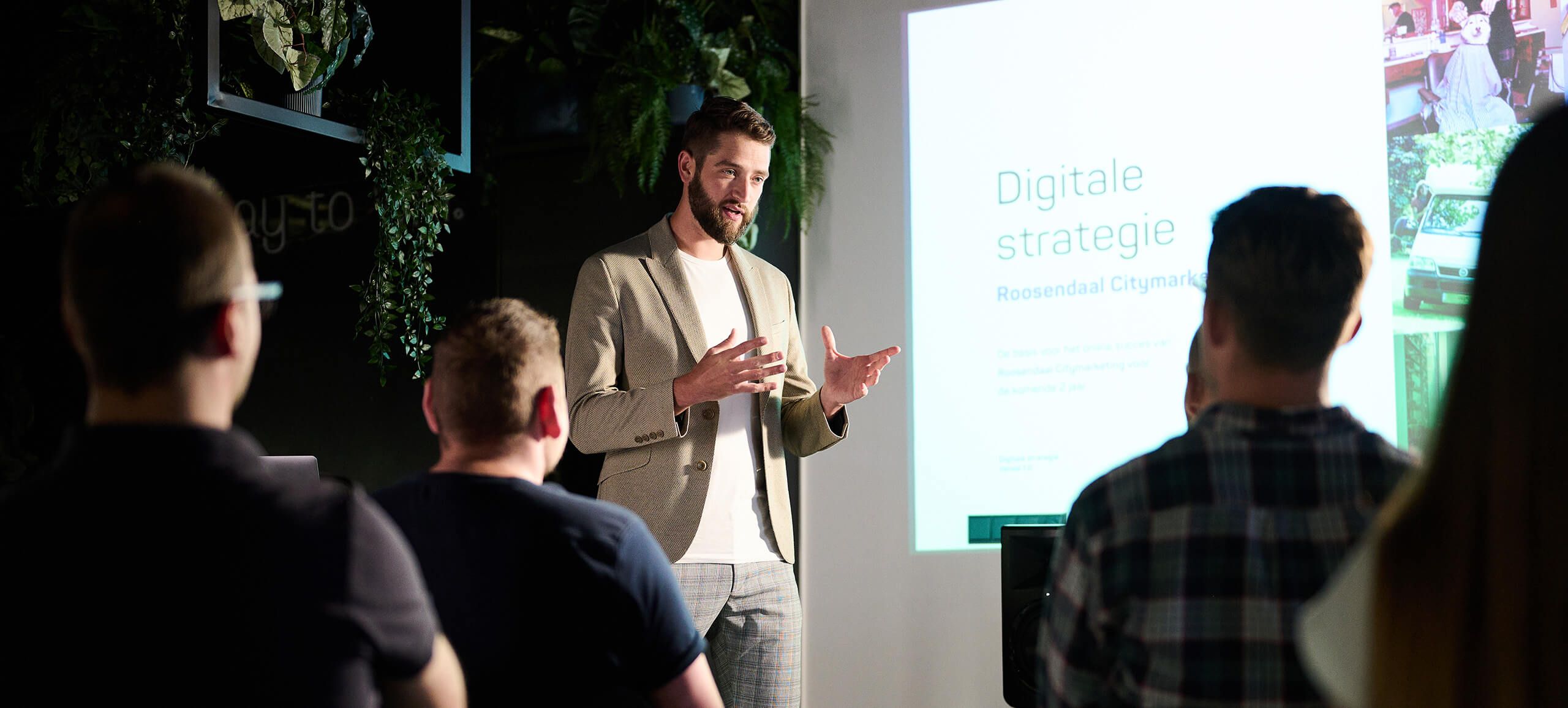 De presentator bespreekt digitale strategie en leadgeneratie aan een kleine groep in een donkere ruimte.