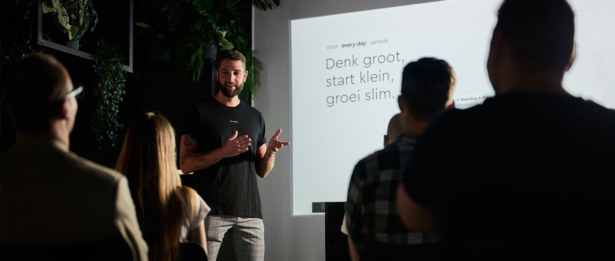Een man presenteert en projecteert de boodschap "Denk groot, begin klein, word slim" waarmee hij het belang van gedragsverandering benadrukt.