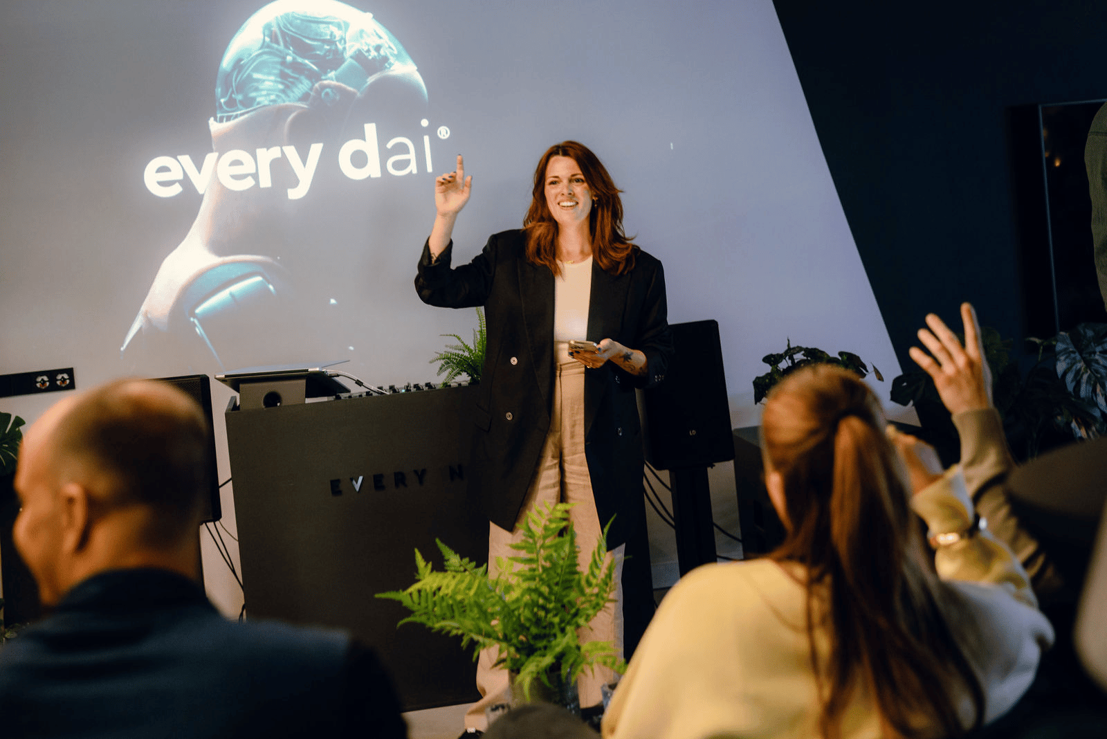 Een vrouw geeft een presentatie aan een publiek, met achter haar op het scherm 'elke dag' strakke, futuristische graphics.