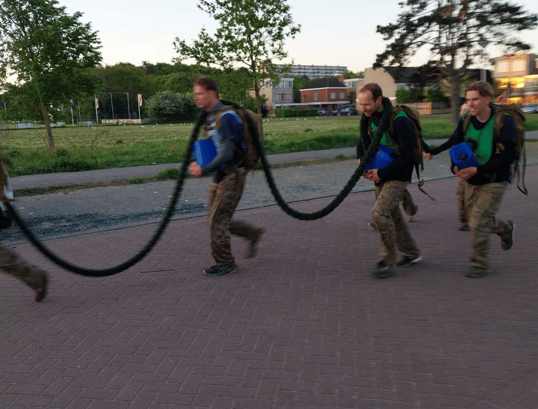 Drie mensen in camouflagebroeken lopen in een rij naar buiten, elk met een dik touw in de hand.