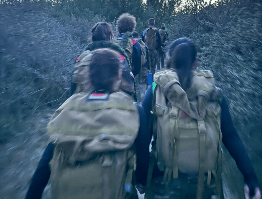 Soldaten lopen bij zonsondergang door het bos, van achteren gefotografeerd.