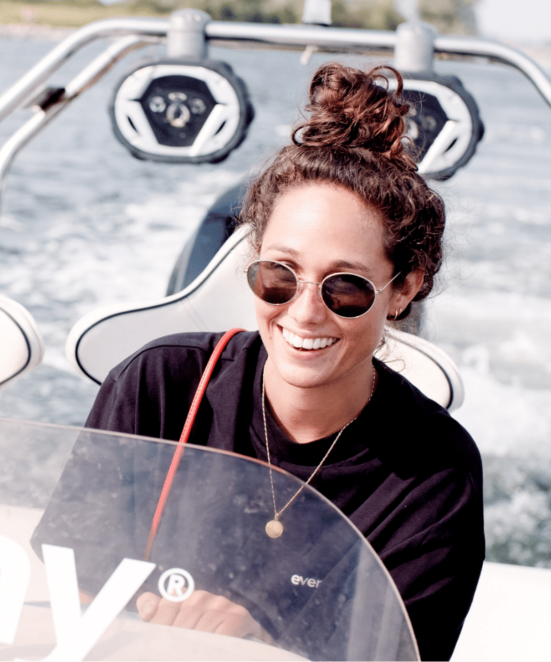 Zonnebril op, rommelige knot op, glimlachend terwijl ze de boot besturen in de zon.
